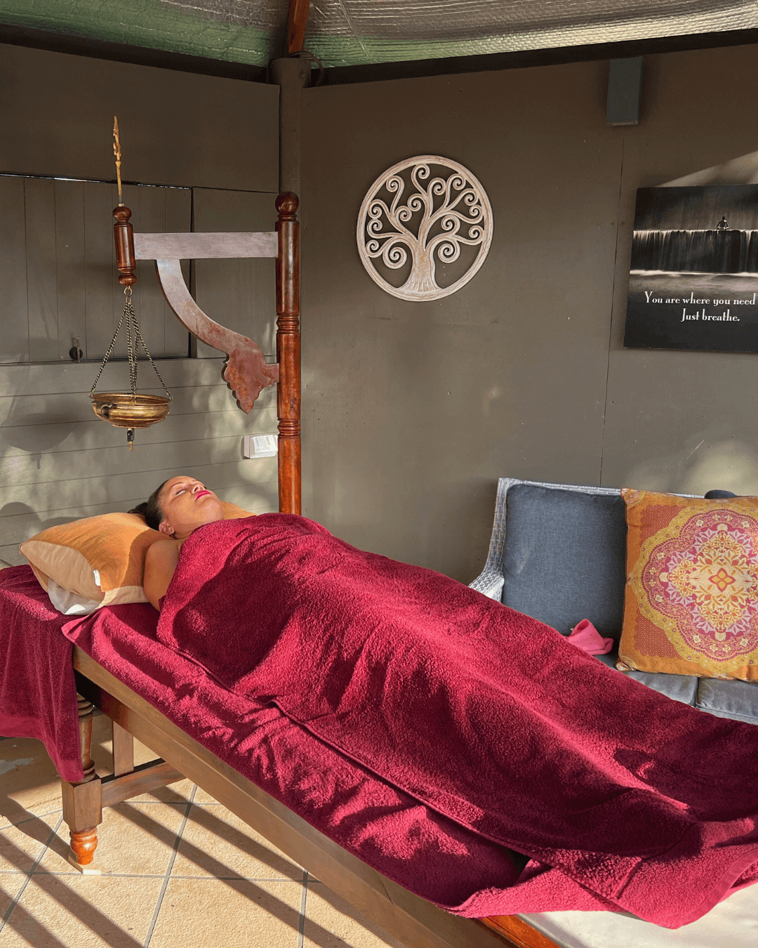 Shirodhara Treatment – Rebirth: A 4-Week Awakening A woman rests peacefully during a traditional Ayurvedic treatment beneath a golden oil vessel, wrapped in a soft burgundy blanket at Unity Yoga Ayurveda Mackay, part of the Rebirth: A 4-Week Awakening program for relaxation and renewal.