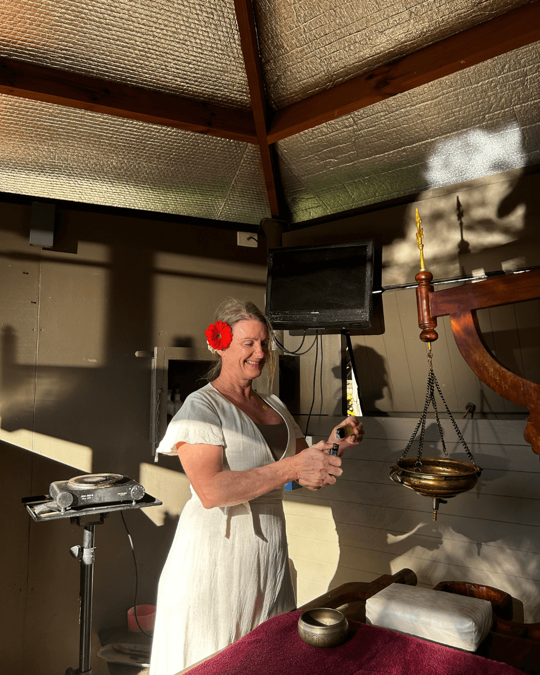 Ayurvedic Ritual with Susan Deakin – Rebirth Program A smiling yoga and Ayurveda practitioner preparing herbal oils for a traditional treatment at Unity Yoga Ayurveda Mackay, symbolizing care, warmth, and holistic renewal in the Rebirth: A 4-Week Awakening program.