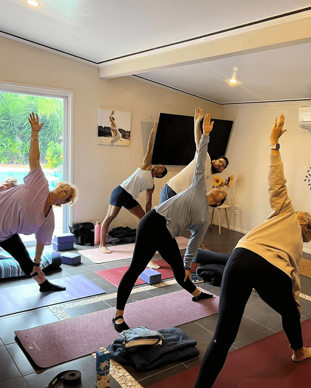 Yoga Class – Rebirth: A 4-Week Awakening A small group practicing yoga in a bright studio overlooking tropical gardens, guided by a yoga teacher at Unity Yoga Ayurveda Mackay — part of the Rebirth: A 4-Week Awakening renewal journey.