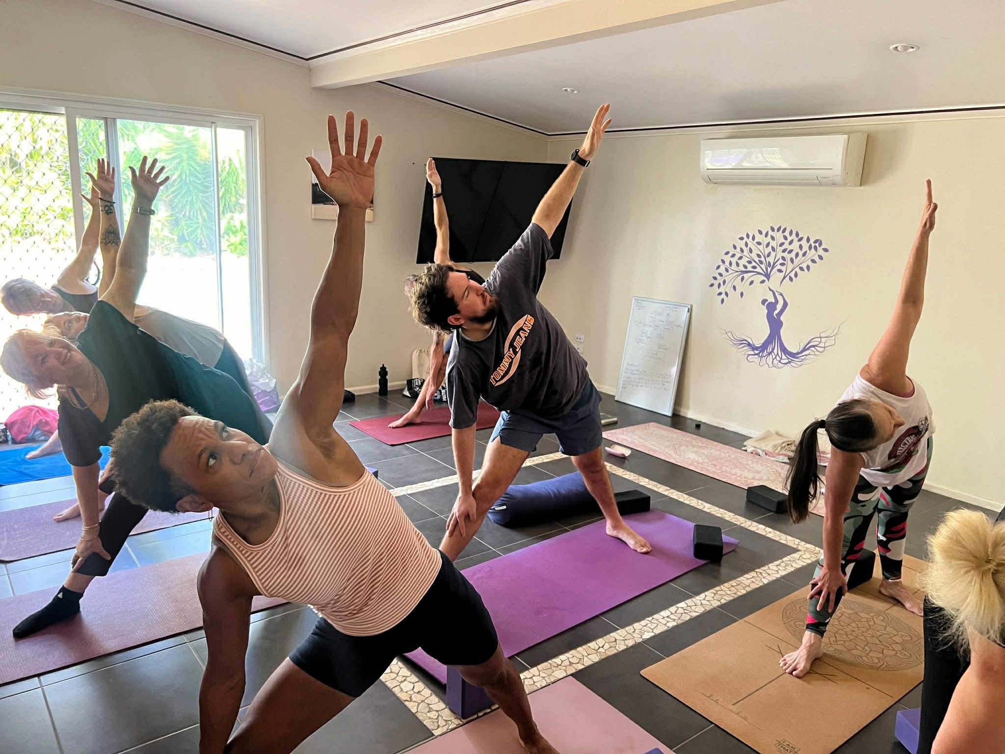 Mixed-gender yoga class practising a standing side stretch during a yoga teacher training session at Unity Yoga Ayurveda in Mackay, Queensland.